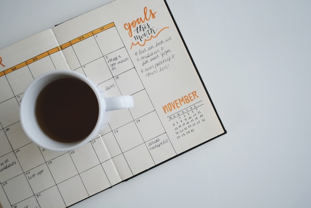 Tavoitteet kirjattuna kalenteriin, joka on pöydällä kahvikupin kanssa.